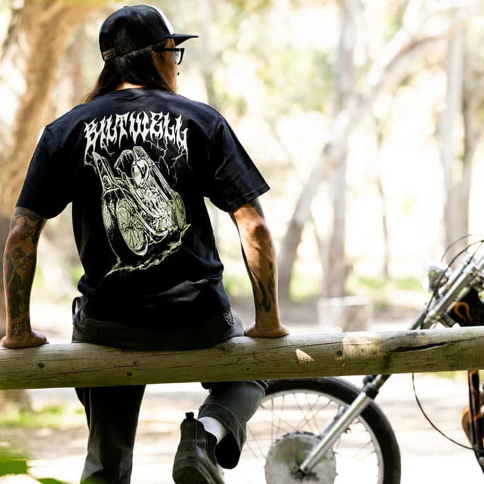 Man med motorcykel-tshirt sitter på en stock bakom en motorcykel.